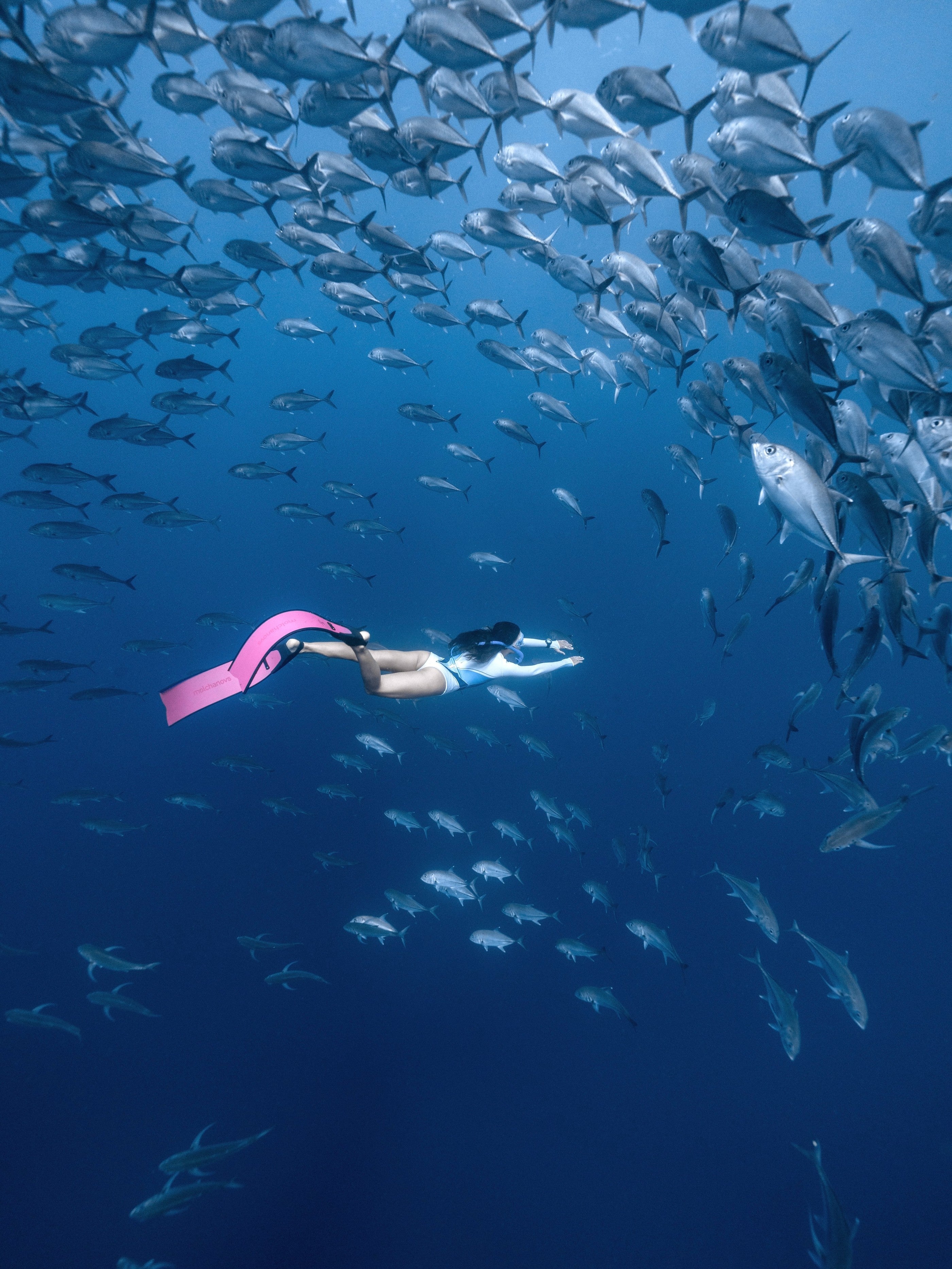 Woman in Yanita springsuit swimming with pink fins among fish underwater