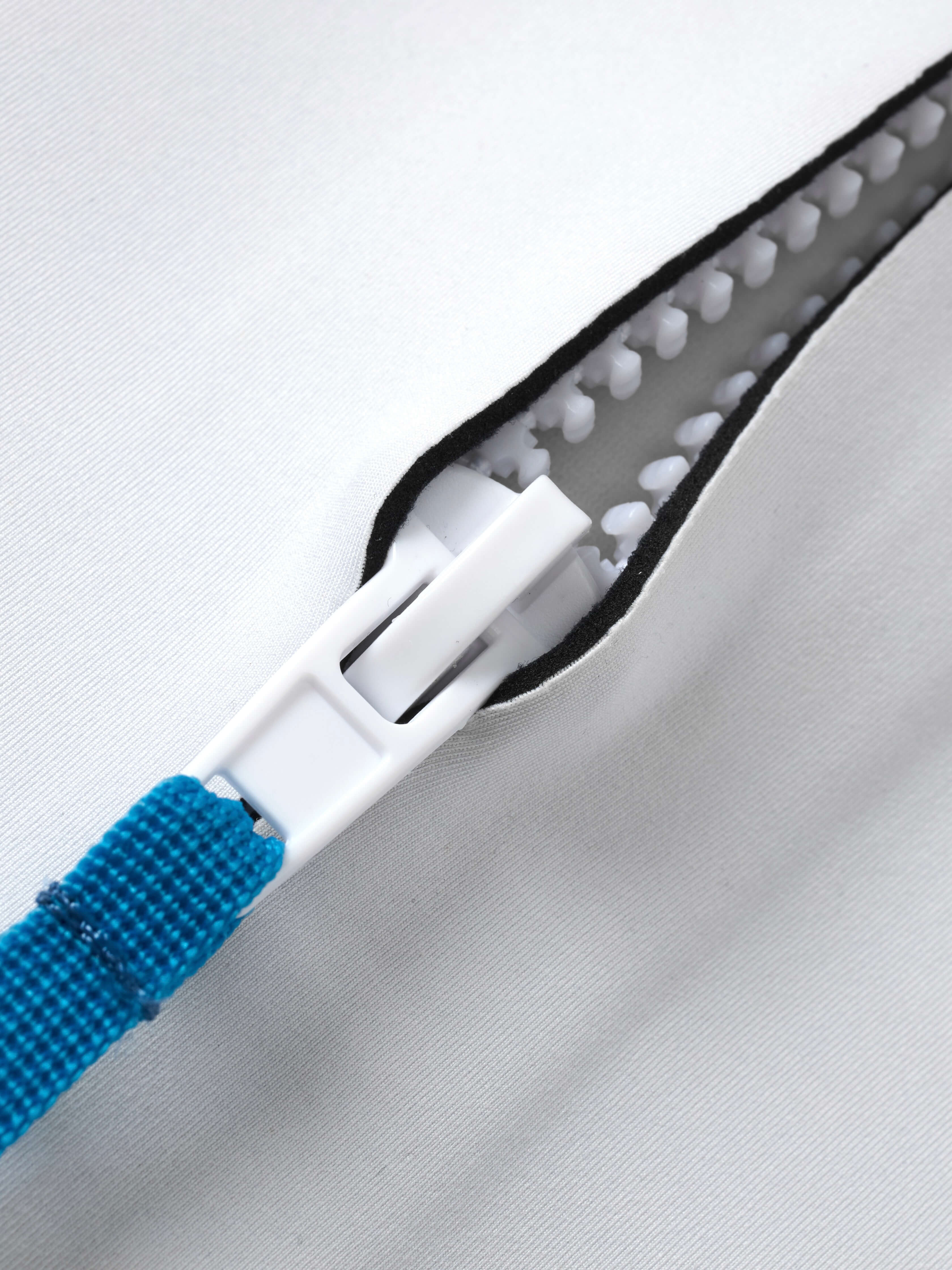 Yanita springsuit back zipper close-up showing white plastic zip teeth, blue pull tab, and internal neoprene lining