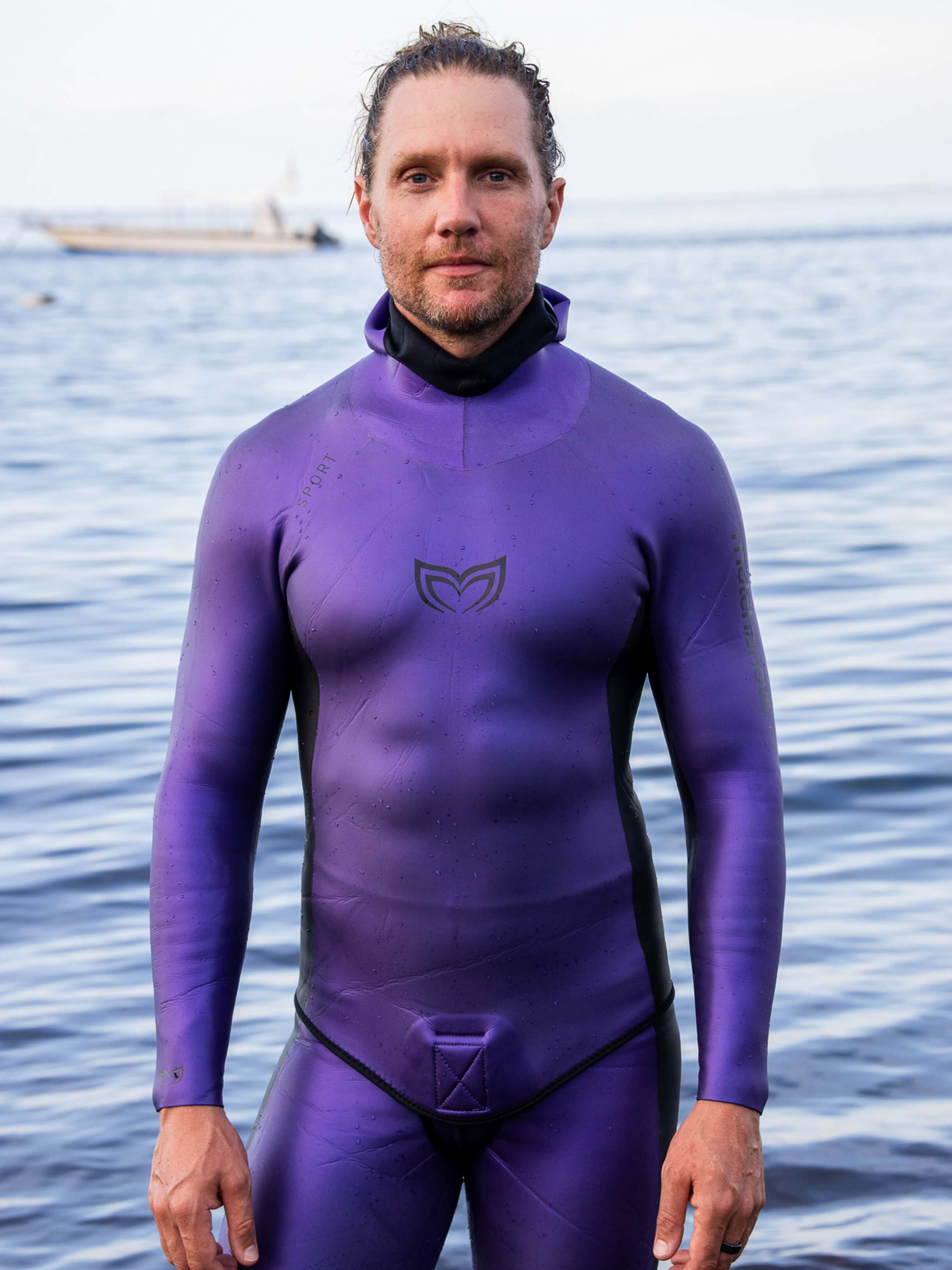 Male freediver wearing the Molchanovs Natalia's Legacy purple SPORT wetsuit 1.5mm, standing at the water's edge