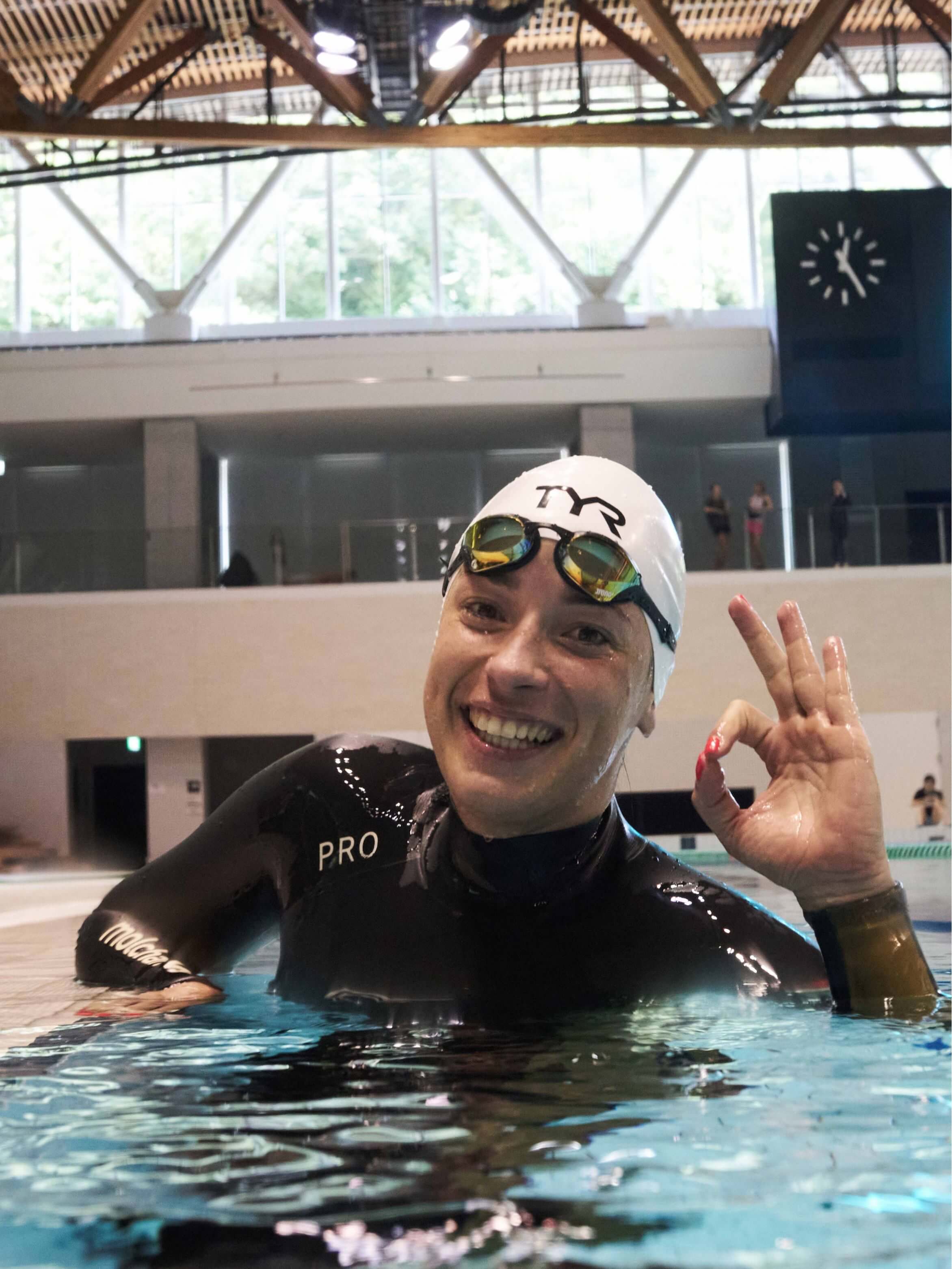 Freediver in a black Molchanovs PRO one-piece wetsuit smiling at the pool wall during a competition