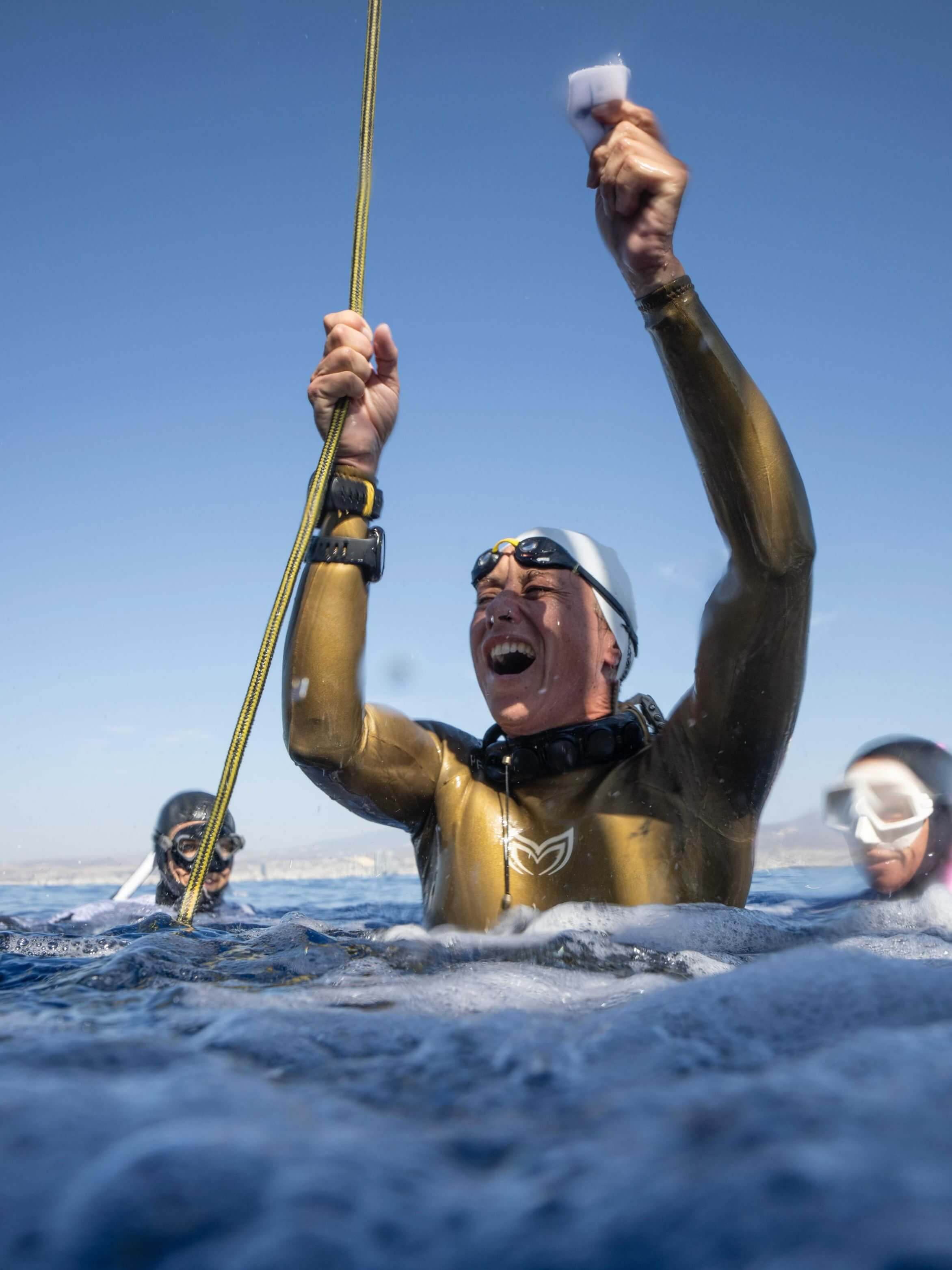 Freediver in a gold Molchanovs PRO wetsuit surfacing and celebrating after an open-water dive
