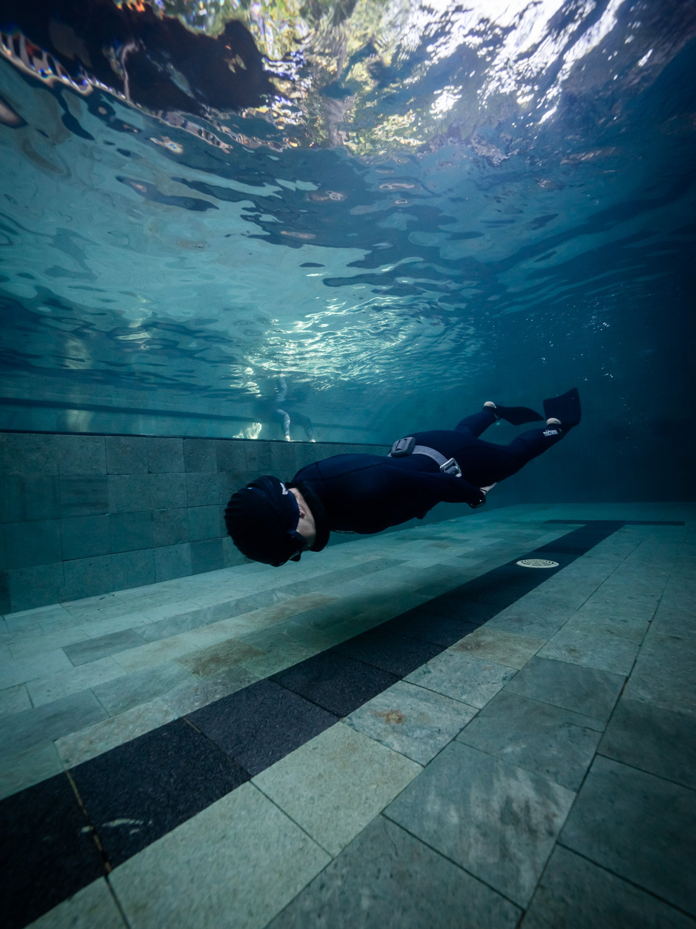 Freediver gliding underwater along a pool floor wearing a Molchanovs CORE wetsuit and bifins