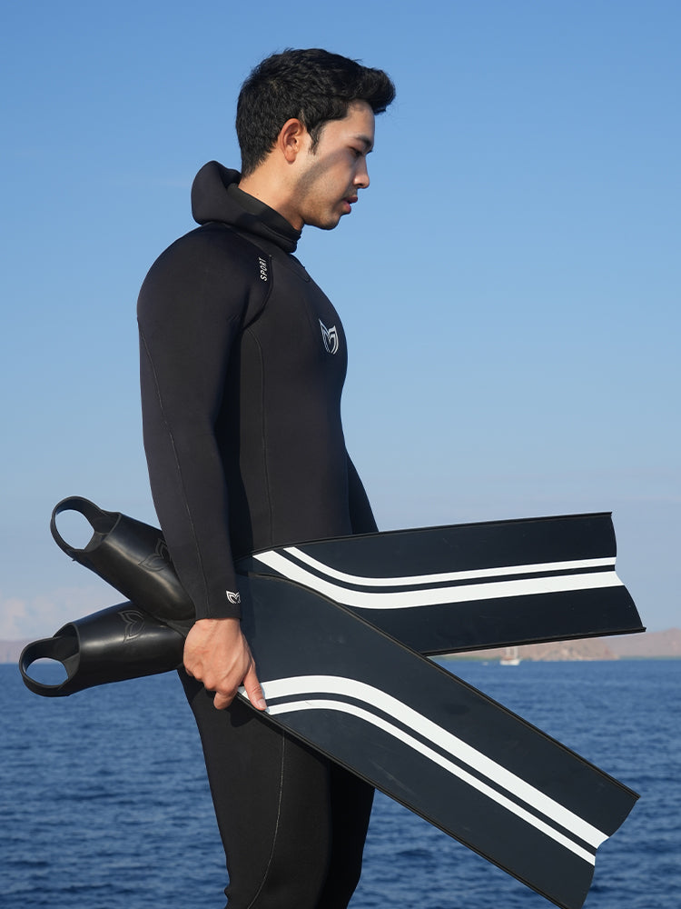 Freediver in Molchanovs Sport wetsuit holding PRO Bifins 3 Fiberglass blades outdoors at the water's edge