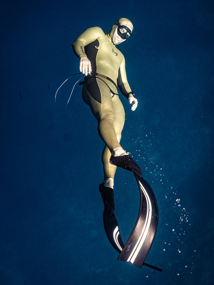 Freediver in Molchanovs wetsuit kicking upward in open blue water wearing PRO Bifins 3 Carbon with white stripe