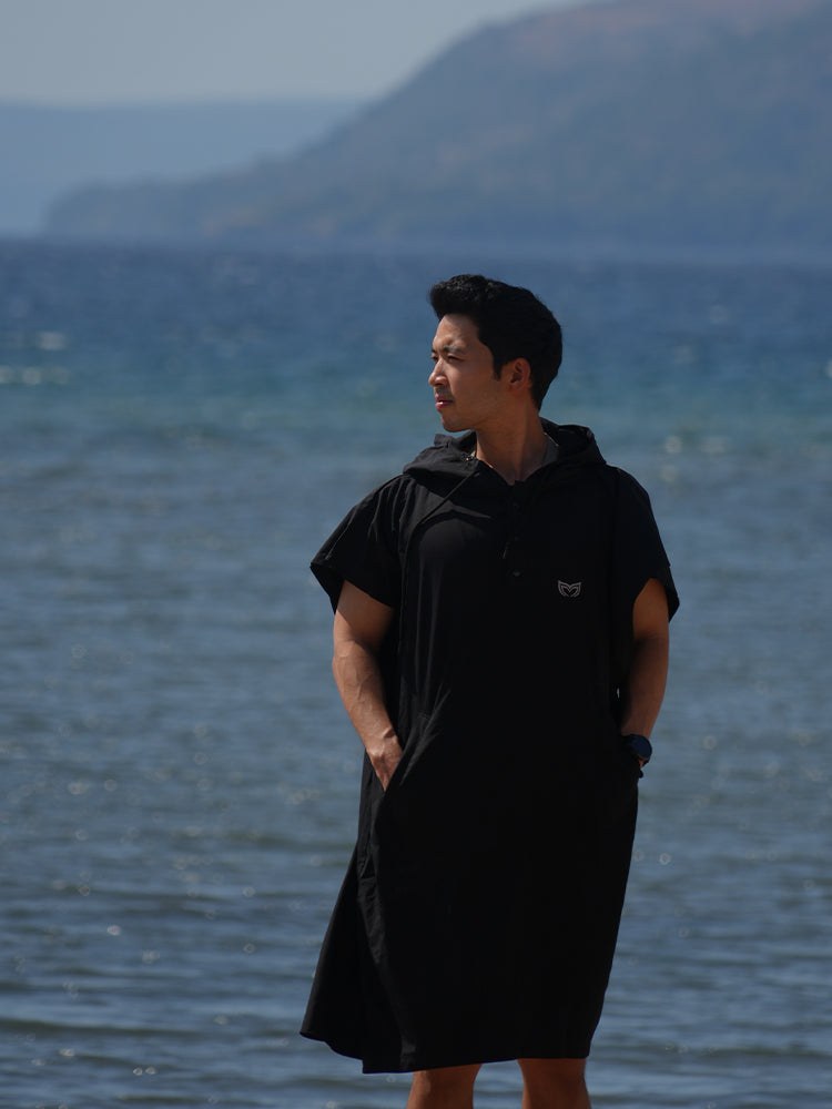 Man wearing Molchanovs black poncho towel at the waterfront after a freedive session