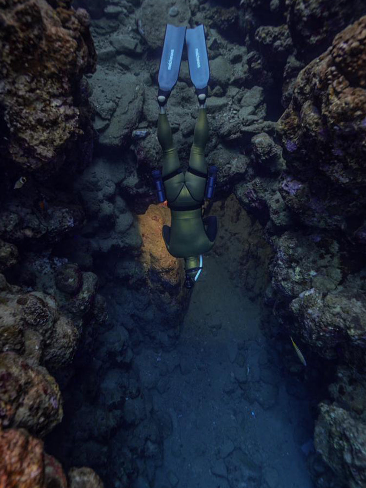 Freediver navigating a narrow reef passage wearing Molchanovs carbon bifins with blue stripes