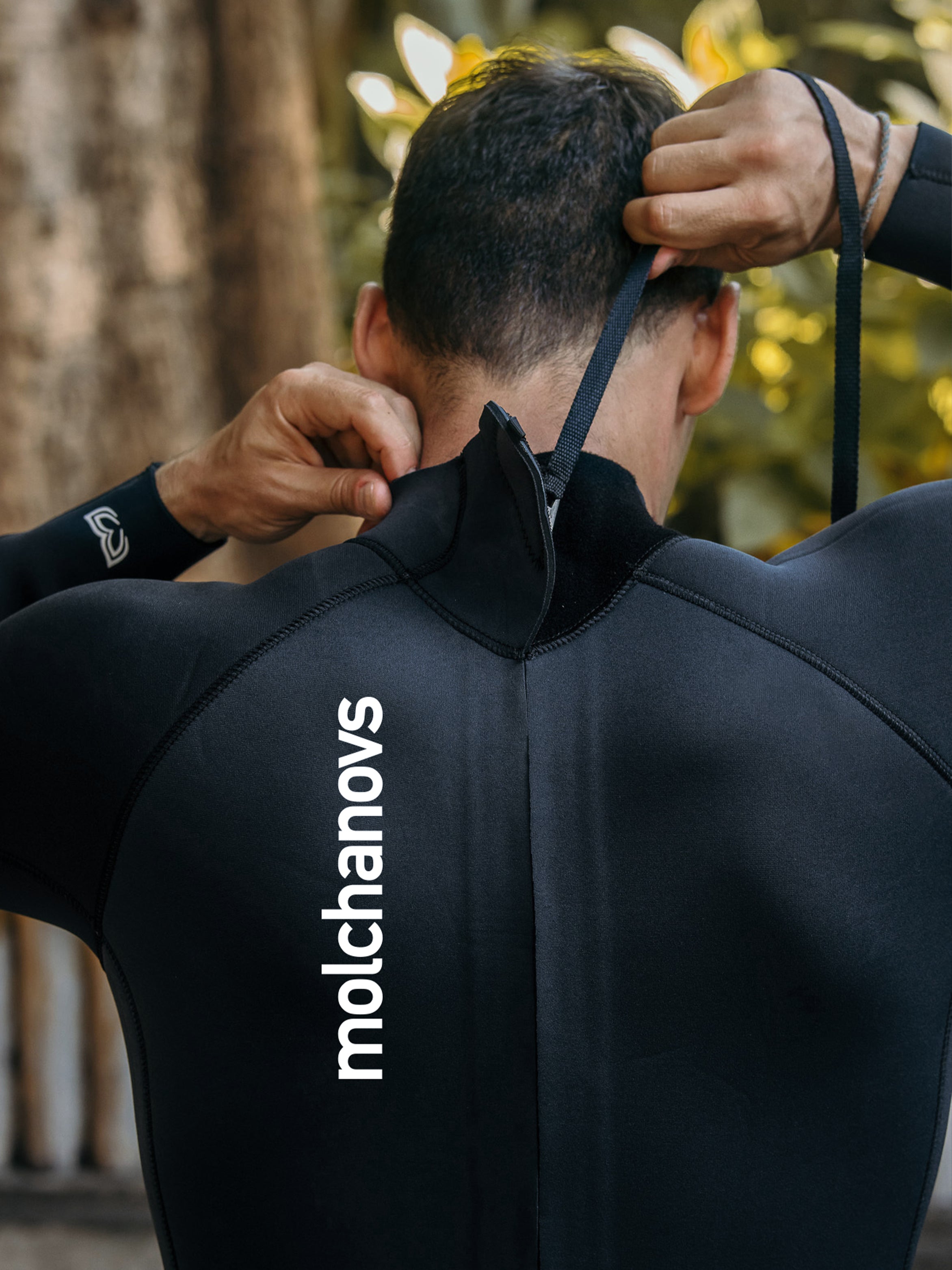 Rear view of male freediver zipping up the Molchanovs CORE one piece wetsuit, showing the back zip pull and molchanovs branding