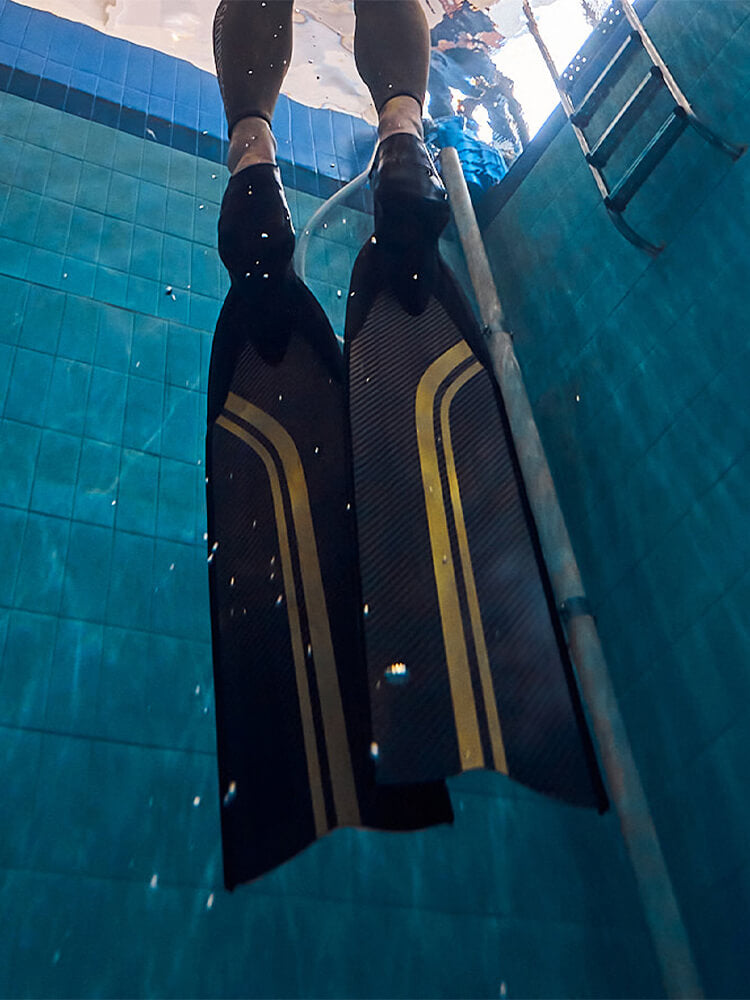 Underwater pool shot looking up at a freediver wearing Molchanovs PRO Hyper Carbon Bifins with gold stripe, entering the water