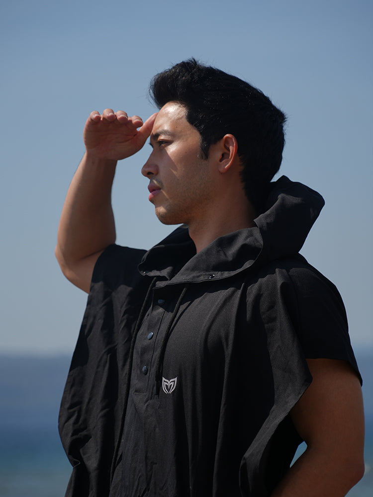 Close-up of man wearing Molchanovs black poncho towel outdoors, showing hood and snap button detail