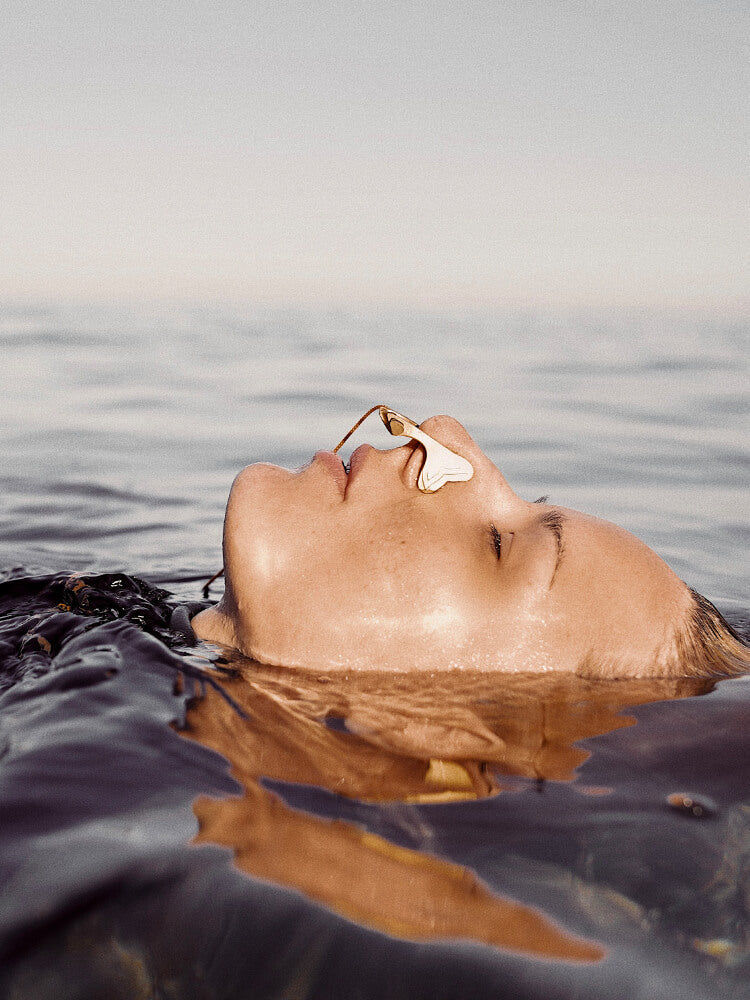 Freediver floating face-up on the water surface wearing the Molchanovs A6063x nose clip in gold, showing the clip in use