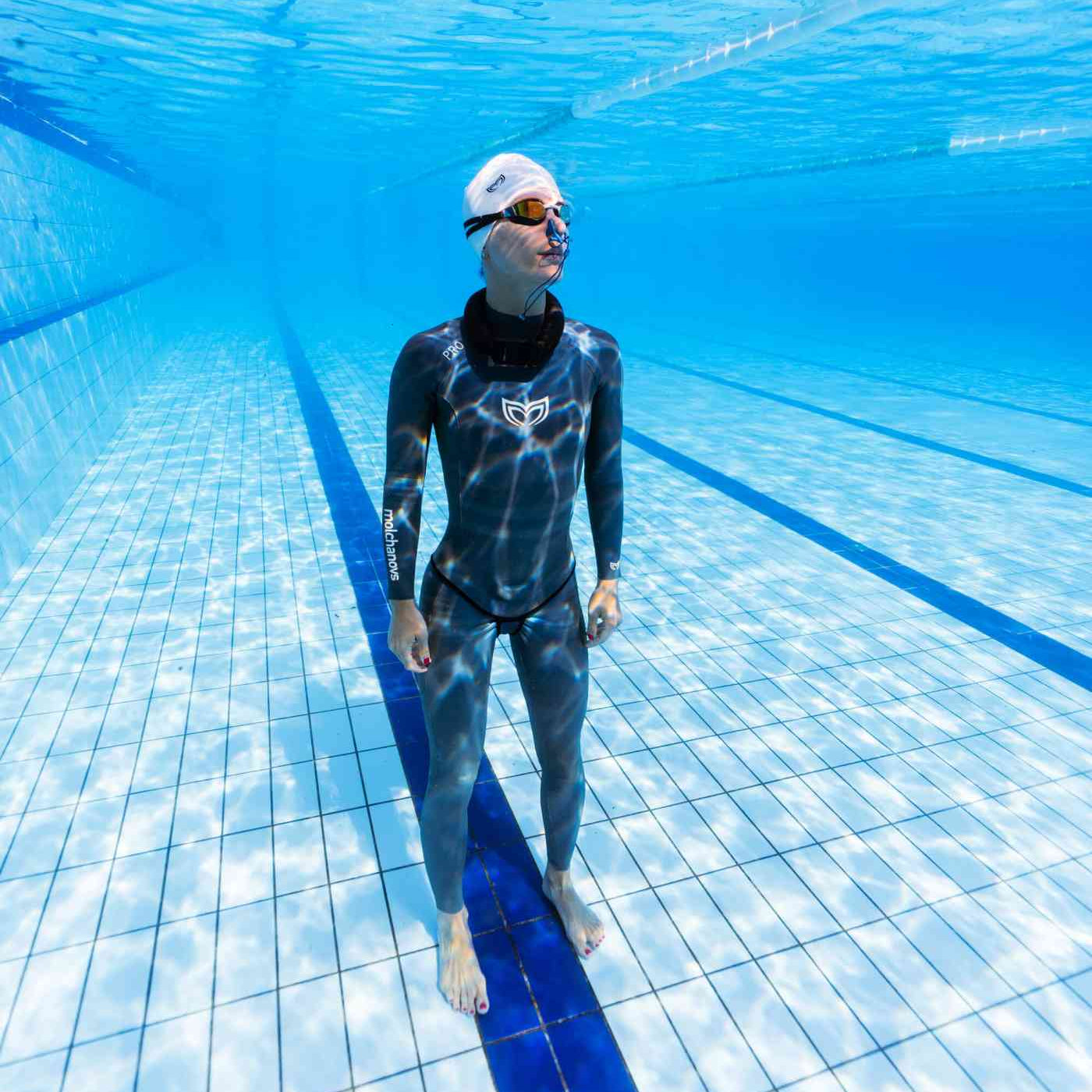 Female freediver in a Molchanovs two-piece wetsuit standing on the floor of an indoor pool