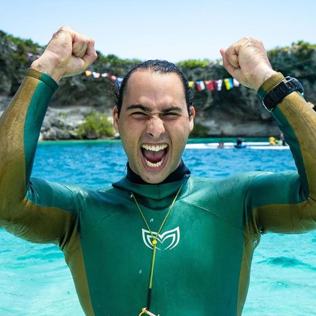 Freediver in a green Molchanovs wetsuit celebrating at the surface after a successful dive