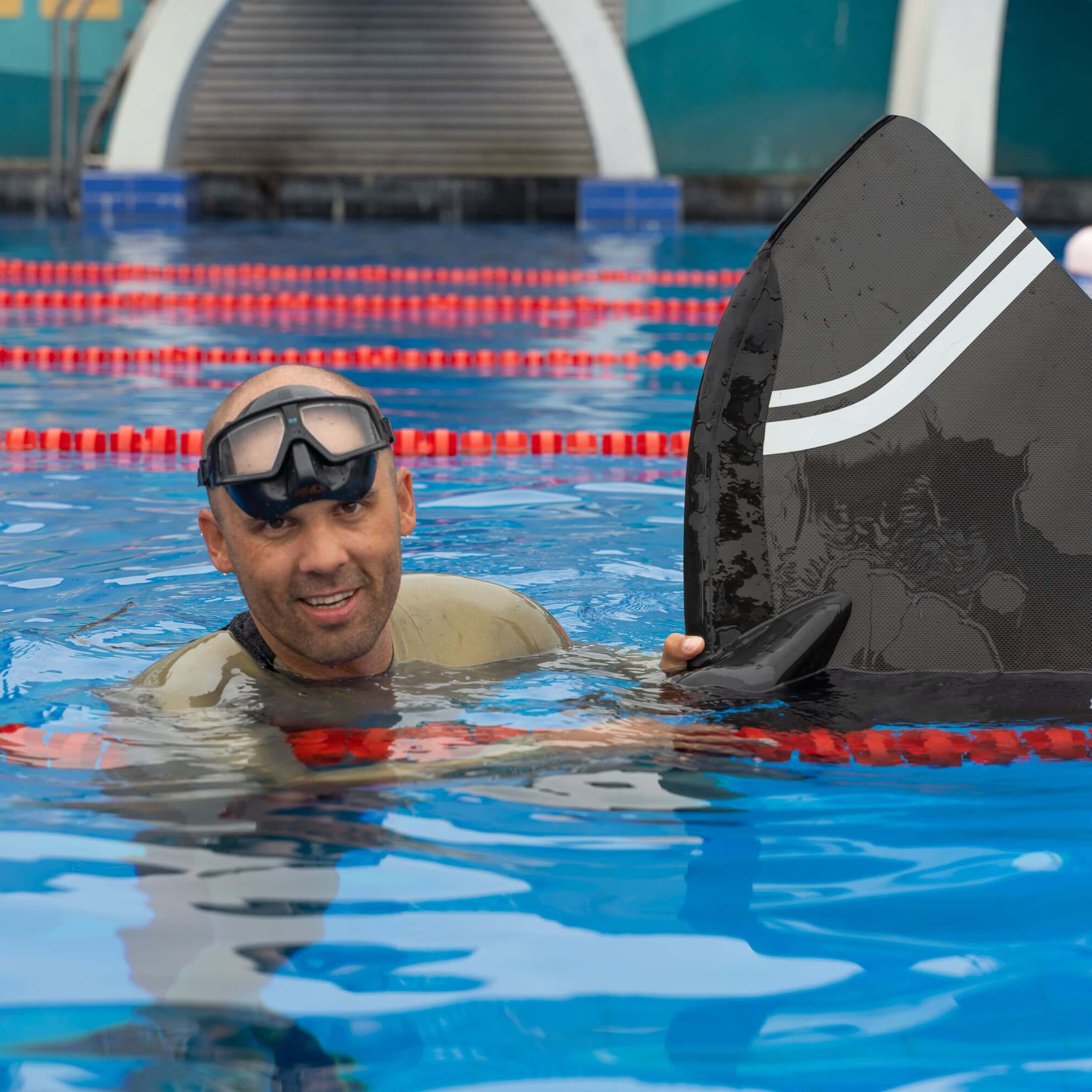 Freediving instructor holding a monofin at the surface of an indoor pool during a training session