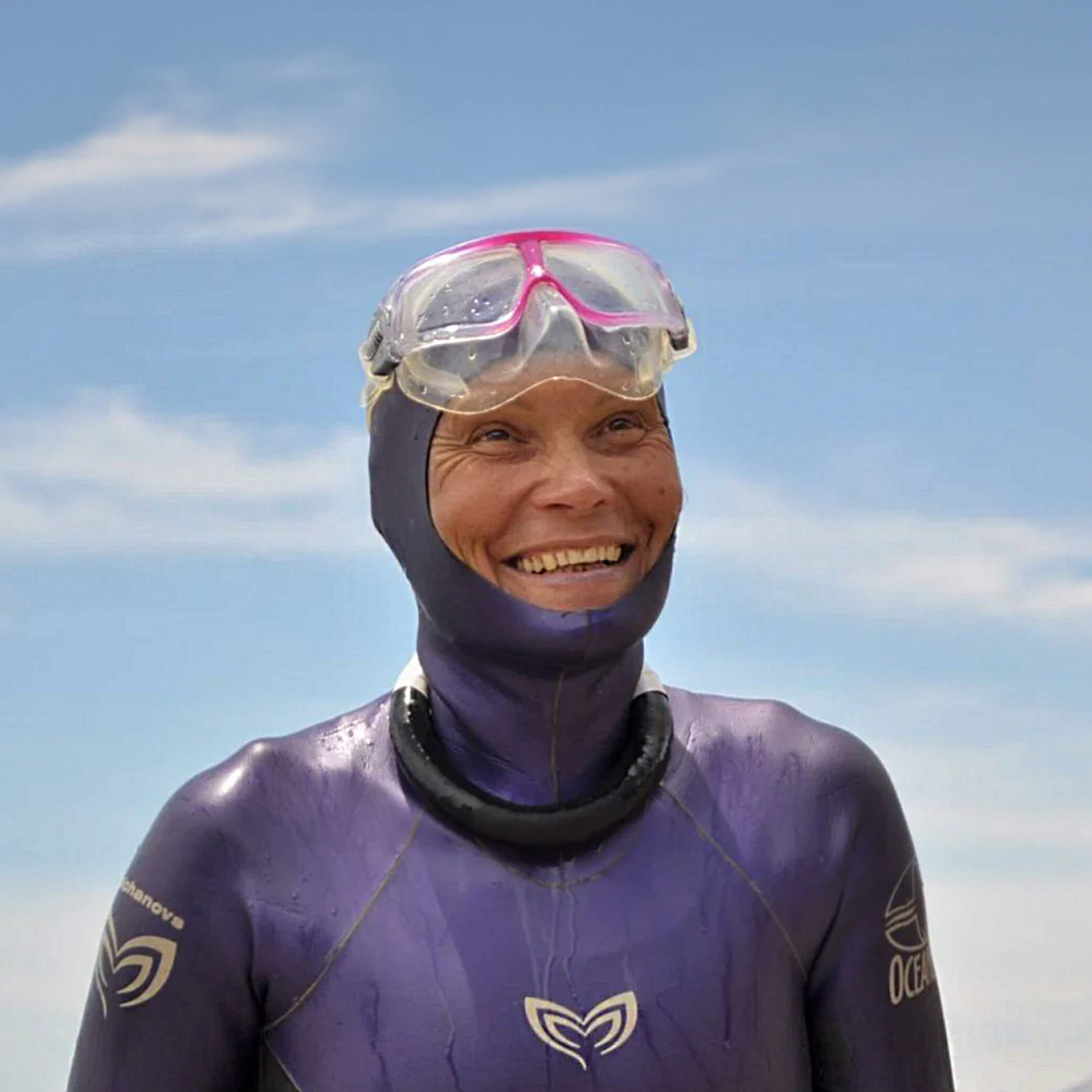 Natalia Molchanova smiling in her signature purple Molchanovs freediving wetsuit and pink-framed mask outdoors