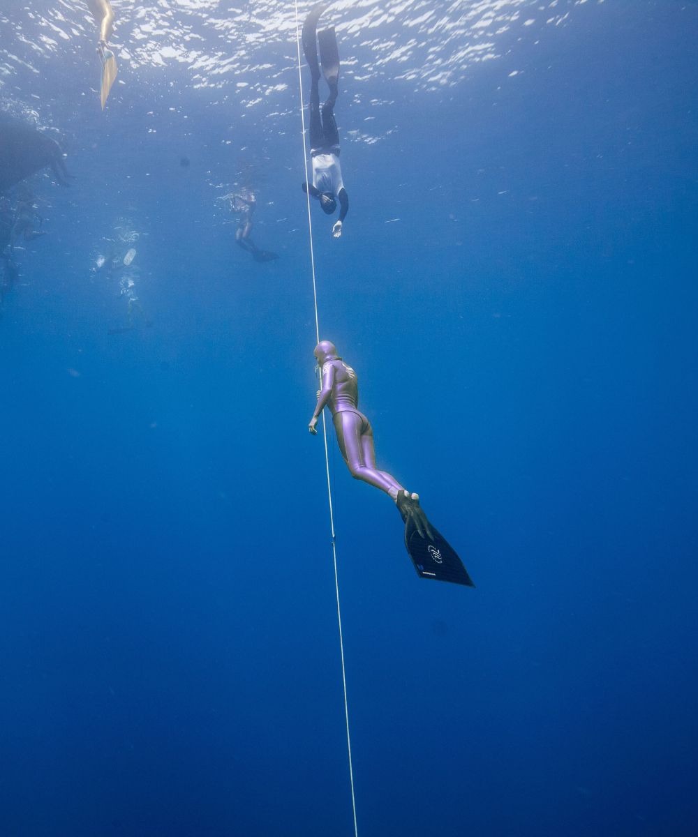 Freediver in a purple wetsuit descending along a dive line in open ocean, Natalia Legacy Collection mobile banner